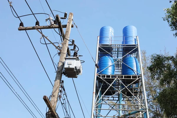 Plastic water reserve tank on the tower. Blue plastic water tank on tall metal structure with electric support system on green tree and blue sky background with copy space and selective focus.
