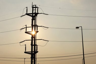 Silhouette of twin electric poles at sunset. View of electric tower with high voltage switch fuses in evening with sun on dim sky background with copy space and focus.