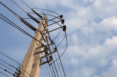 İkiz sütunlarda yüksek voltajlı elektrik hatları. Gökyüzü arka planında yüksek voltaj iletim hattına sahip elektrik direğine yakın çekim alanı ve odak noktası olan alttaki beyaz bulutlar.