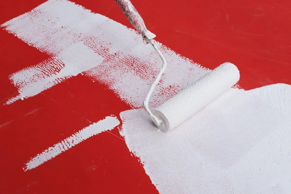 White paint roller on a red wall. Renovating an old wall using a long-handled roller paint white over a red background.