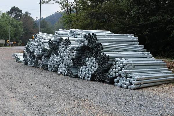 A pile of metal poles on the side of the road. Pile of silver steel poles on gravel pavement beside road for construction of guard rail curved mountain road and selective focus.