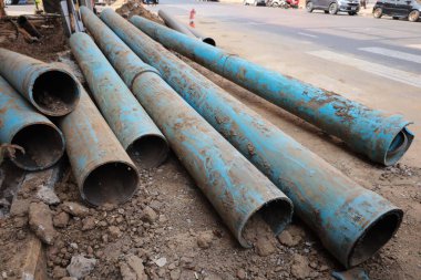 Yolun kenarındaki eski su boruları. Kopya alanı ve seçici odaklı inşaat alanında asfaltlı yol arkaplanındaki kentsel alanda bozulmuş ve kırılmış mavi PVC tesisat boruları yığını.