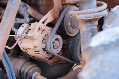 Kirli araba şarj dinamosu. Eski alternatörü kırmızı tozla kapatıyoruz. Eski kemer, seçici odaklı, off-road aracının makine dairesinde..