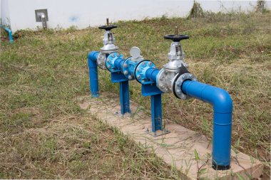 Kontrol vanaları ve endüstriyel su sayaçları. Fabrika binasına ya da çimento sahasında fotokopi alanı olan büyük bir binaya su taşımak için kullanılan mavi metal borulu kelebek valfi. Odaklanmayı seç