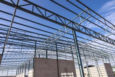 Metal warehouse roof structure. Detail of industrial steel roof structure workshop under construction on blue sky background with thin white clouds and selective focus. clipart