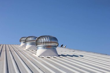 Çatıda havalandırma vantilatörü var. Endüstriyel fabrika çatısında mavi gökyüzü arka planındaki depoya soğuk hava taşımak için seçici bir odak ile dönen üç parlak metal top..