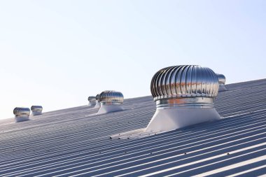 Çatıda havalandırma vantilatörü var. Bir fabrikanın ya da endüstriyel fabrikanın çatısında dönen parlak metal seçici bir odak ile mavi gökyüzü arka planındaki soğuk havayı kontrol etmek ve dolaşmak için kullanılır..