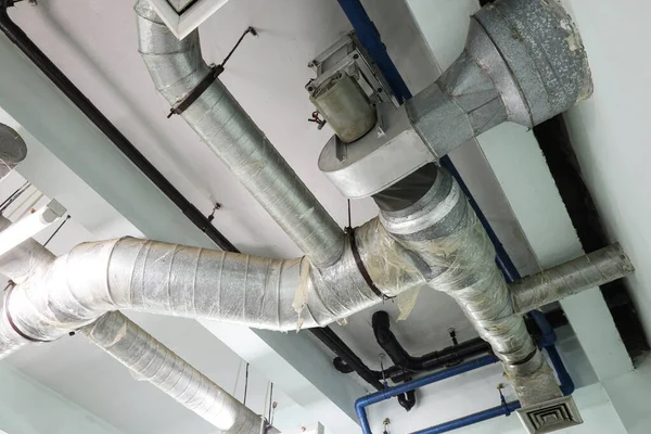 Air conditioning pipes on the ceiling. Close up of silver metal duct system with motor for controlling indoor ventilation on dirty room ceiling background with copy space with selective focus.