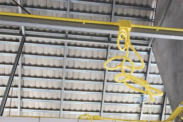 Boxes and electrical conduits on steel frames. Yellow cable conduit hanging from house rafters as electrical and communication system during construction in bottom view with selective focus.