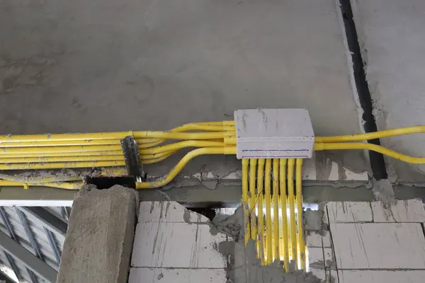 Boxes and electrical conduits on the wall. Yellow plastic cable conduit connection box hanging on cement wall of electrical system in house under construction with selective focus.
