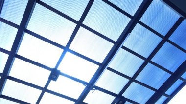 Şeffaf çatı. Gökyüzü arka planında şeffaf çatı tavanının siyah çelik yapısı ve seçici bir odak ile en altta parlayan güneş..