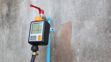 Otomatik su sayacı. Aşağıdaki eski beton duvarın arka planındaki musluğa ve hortuma bağlı siyah otomatik sulama zamanlayıcısını fotokopi alanı ile kapatın. Seçici odak