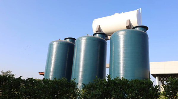 Три резервуара для пластиковой воды. Темно-зеленые резервуары для хранения воды из стекловолокна на открытом воздухе для хранения воды на белом фоне резервуара для воды и под низким углом неба с копировальным пространством. Селективный фокус