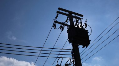 Transformatörün silueti direkte. Aşağıda düşük voltajlı kablolu üç aşamalı transformatör ve mavi gökyüzü arka planında öğleden sonra güneşi ve metin için uzayı kopyalamak. seçici odak