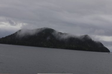 Juneau, Alaska 'da bir limanda, kar kaplı bir dağ ve arka planda alçak bir sis bulunan bir yolcu gemisi.