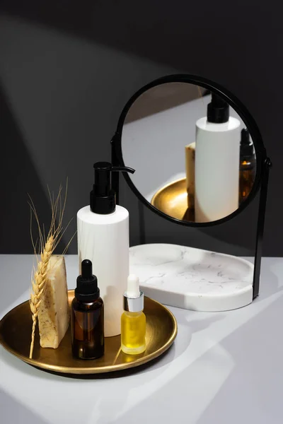 Creative still life with organic cosmetics. Set of essential oils, handmade soap and mirror on a dark gray background. The concept of selfcare and organic products. Reflection in the mirror.