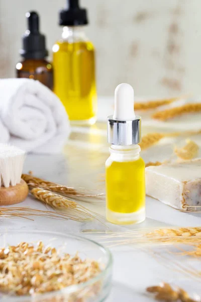 Oils, bath brush, towel and wheat sprouts on the cosmetic table in the bathroom. A set of organic cosmetics in glass vials with dropper for skin and hair care. The concept of self care and spa.
