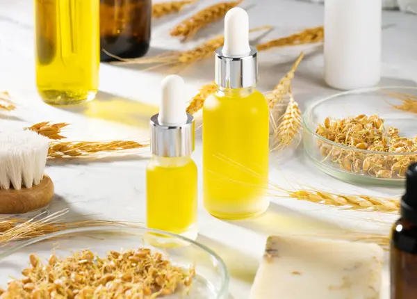 Wheat serum oil for skin and hair care. A conceptual composition of wheat essential oils, a bath brush and wheat germ on a marble table. Bottle of body oil with a dropper. Self-care, spa and wellness.