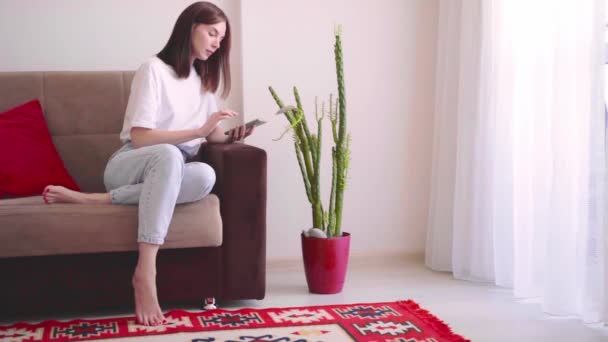 年轻美丽的女性博主花匠坐在家里的沙发上 手持智能手机 为社交媒体拍照 讲述植物疾病 室内植物疾病的识别和治疗 — 图库视频影像