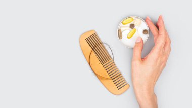Kadın elinde serum olan kozmetik ampuller, saç uzatmak için vitaminler, güzel saçlar. Gri arka planda saç kaybı olan tahta tarak. Saç kaybı, kellik sorunu kavramı. Düz taban. Boşluğu kopyala