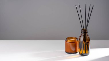Aroma yayıcı, doğal yağ, kehribar rengi soya mumu, kahverengi cam şişe ve beyaz gri arka planda kavanoz. Sürdürülebilirlik, akıl sağlığı ve uyum kavramını benimse. Uzayı kopyala Pankart.
