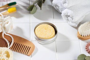 Beyaz seramik arka planda duran sürdürülebilir sağlam şampuan barı ve banyo aksesuarları. Eko dostu saç bakımı. Plastiksiz, sıfır atık, düşük su malzemesi. Ev banyosu yaşam tarzı kompozisyonu.