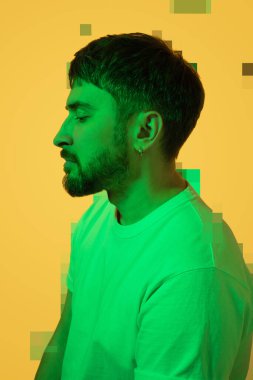 Sakallı, orta yaşlı bir adamın yaratıcı portresi. Ruhsal sorunları olan bunalımlı bir adam üzgün bir şekilde aşağıya bakıyor ve dağılıyor. Sarı arka planda renkli yeşil ışık. Orta yaş krizini kabul et.