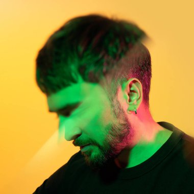 Prizma yoluyla sanatsal yaratıcı portre. Sarı arka planda yeşil, pembe neon ışıklarla bakan bir adam. Kulağında küpe olan, modern fotoğraf yakışıklı, sakallı, orta yaşlı bir adam. Kaleydoskopik etki.