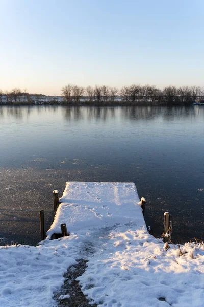Winter landscape with wooden dock covered with snow above the frozen lake