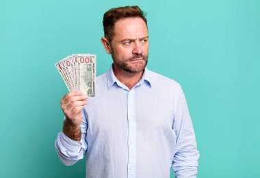 middle age man feeling sad, upset or angry and looking to the side. dollar banknotes concept