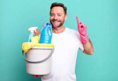 Orta yaşlı bir adam gülümsüyor ve arkadaş canlısı görünüyor. Bir numarayı gösteriyor. Temiz ürünleri olan bir hizmetçi.