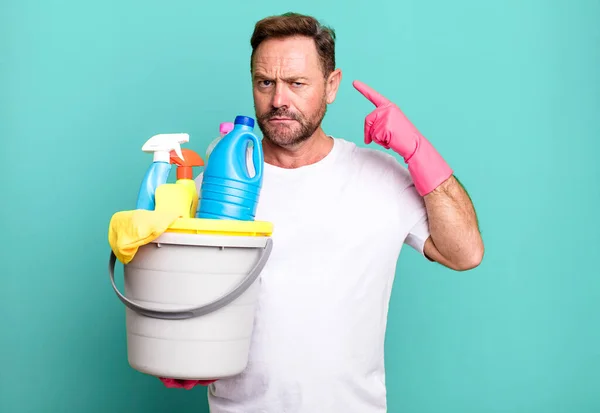 middle age man feeling confused and puzzled, showing you are insane. housekeeper with clean products