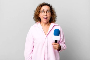 Güzel, orta yaşlı bir kadın çok şaşırmış ya da şaşkın görünüyor. Mikrofon konsepti olan bir TV sunucusu