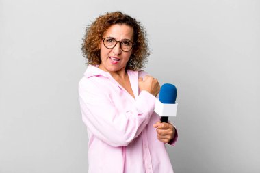 Orta yaşlı güzel bir kadın kendini mutlu hissediyor ve bir meydan okumayla yüzleşiyor ya da kutluyor. Mikrofon konsepti olan bir TV sunucusu