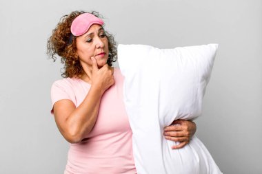 Mutlu, kendine güvenen, elleri çenesinde pijama pijaması ve yastıkla gülümseyen orta yaşlı bir kadın.