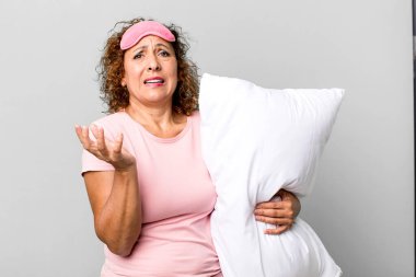 Güzel, orta yaşlı bir kadın umutsuz görünüyor, sinirli ve stresli pijama geceliği ve yastık giyiyor.