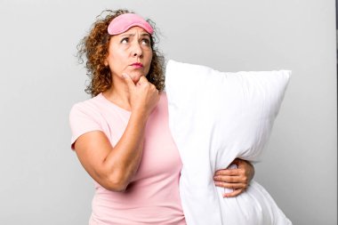 Güzel, orta yaşlı bir kadın pijama giyip yastık takıp kuşkulu ve şaşkın hissediyordu.