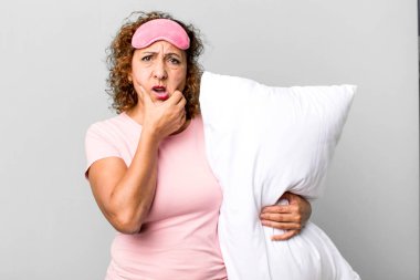 Orta yaşlı, ağzı açık, elleri çenesinde pijama ve yastık giymiş güzel bir kadın.