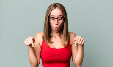 Şok olmuş, ağzı açık ve şaşkın, inançsızlık ve şaşkınlık içinde bakıyor ve aşağı doğru işaret ediyor.