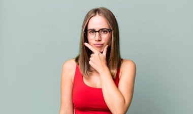 Ciddi görünüyor, düşünceli ve güvensiz, bir kolu çaprazlanmış ve eli çenesinde, seçenekleri değerlendiriyor.