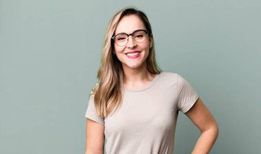 Mutlu bir şekilde gülümsüyor, eli kalçasında ve kendinden emin, olumlu, gururlu ve arkadaş canlısı bir tavırla.