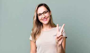 Gülümsüyor ve dost canlısı görünüyor. İki ya da iki numarayı gösteriyor. Elini ileri uzatıp geri sayıyor.