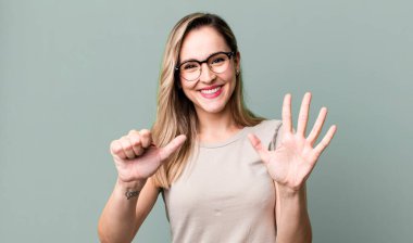 Gülümsüyor ve arkadaş canlısı görünüyor, altı ya da altıncı numarayı gösteriyor, elleri önde, geri sayıyor.