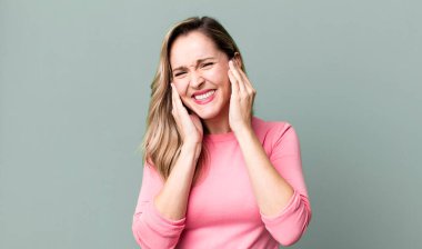 Kızgın, stresli ve sinirli görünüyor, iki kulağı da sağır edici bir ses, ses ya da yüksek sesle kapatıyor.