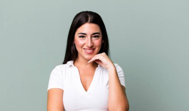 Mutlu görünüyor ve gülümsüyor, elleri çenesinde, merak ediyor ya da bir soru soruyor, seçenekleri karşılaştırıyor.