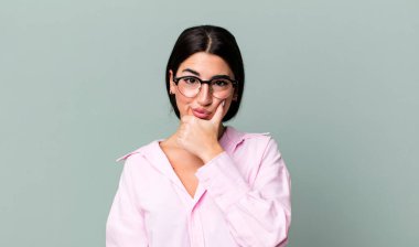 Ciddi görünüyor, düşünceli ve güvensiz, bir kolu çaprazlanmış ve eli çenesinde, seçenekleri değerlendiriyor.