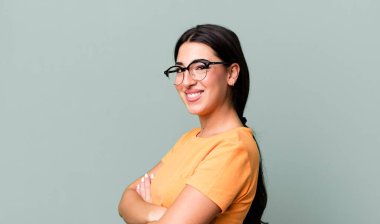 Kameraya çapraz kollarla gülümsüyor ve mutlu, kendinden emin, tatmin olmuş bir ifade, yan görüş.