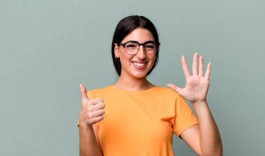 Gülümsüyor ve arkadaş canlısı görünüyor, altı ya da altıncı numarayı gösteriyor, elleri önde, geri sayıyor.