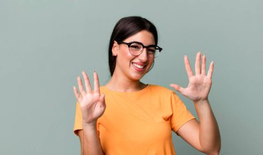 Gülümsüyor ve dost canlısı görünüyor, 9 ya da 9 numarayı gösteriyor, eli önde, geri sayıyor.