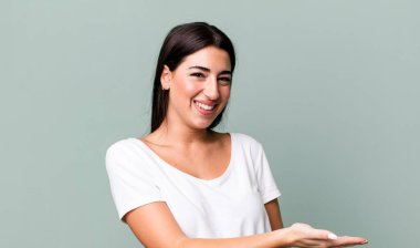 Neşeli bir şekilde gülümsüyor, mutlu hissediyor ve bir konsepti fotokopi uzayında avuç içiyle gösteriyor.